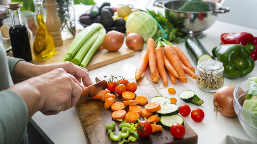 Person chopping colorful vegetables on cutting board with fresh produce and ingredients on counter