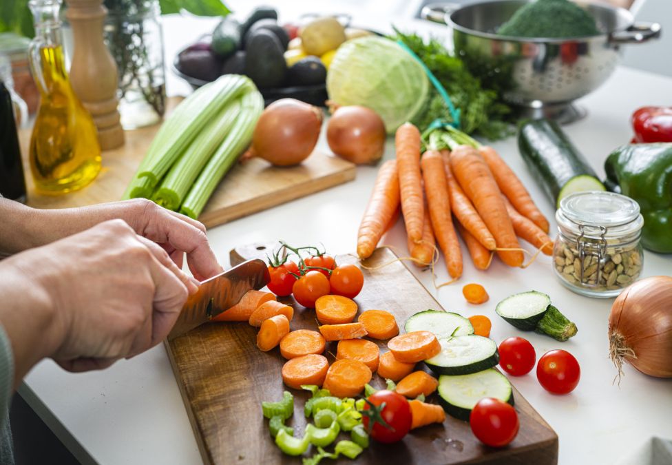 Person chopping colorful vegetables on cutting board with fresh produce and ingredients on counter
