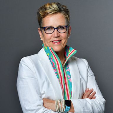 Professional woman in white chef's coat wearing glasses and three medals, arms crossed