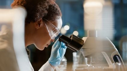 Woman with curly hair looking through microscope in laboratory setting