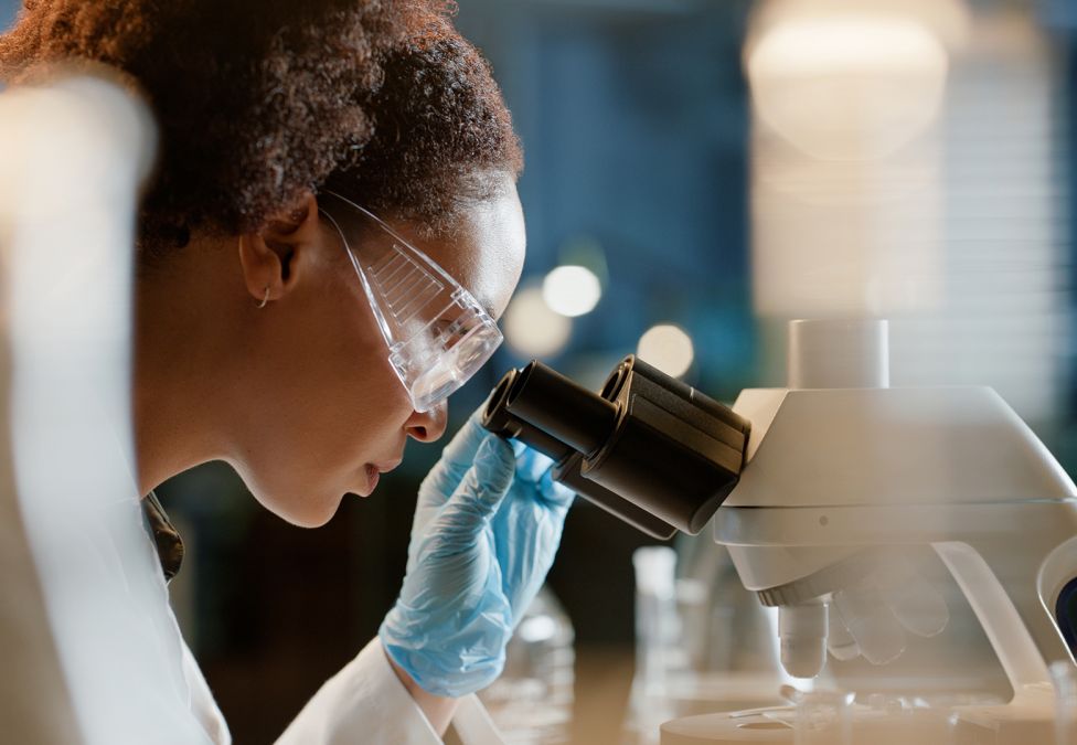 Woman with curly hair looking through microscope in laboratory setting