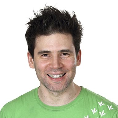 Smiling man with dark hair wearing a green t-shirt against white background
