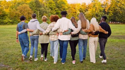 An image of a group of people, facing their backs. They are a diverse group of adult people walking with their arms around each other through a field, leading to an article from the Milken Institute titled "How Philanthropy Can Support a Community-Centered Biomedical Research Ecosystem to Achieve Health Equity".