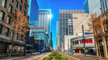 Downtown city street with modern skyscrapers and small businesses under blue sky