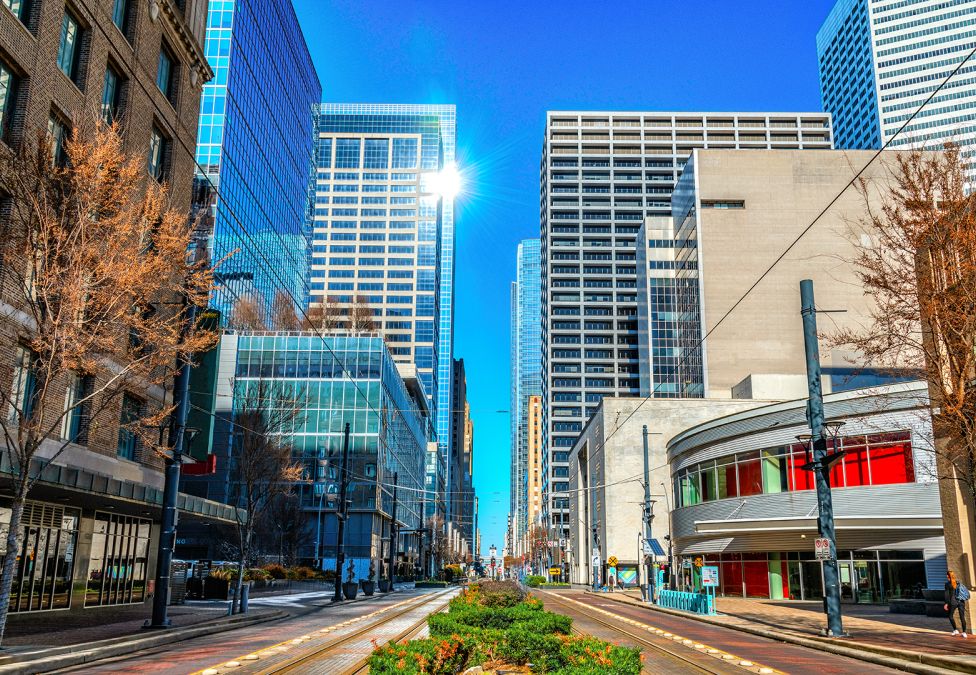 Downtown city street with modern skyscrapers and small businesses under blue sky