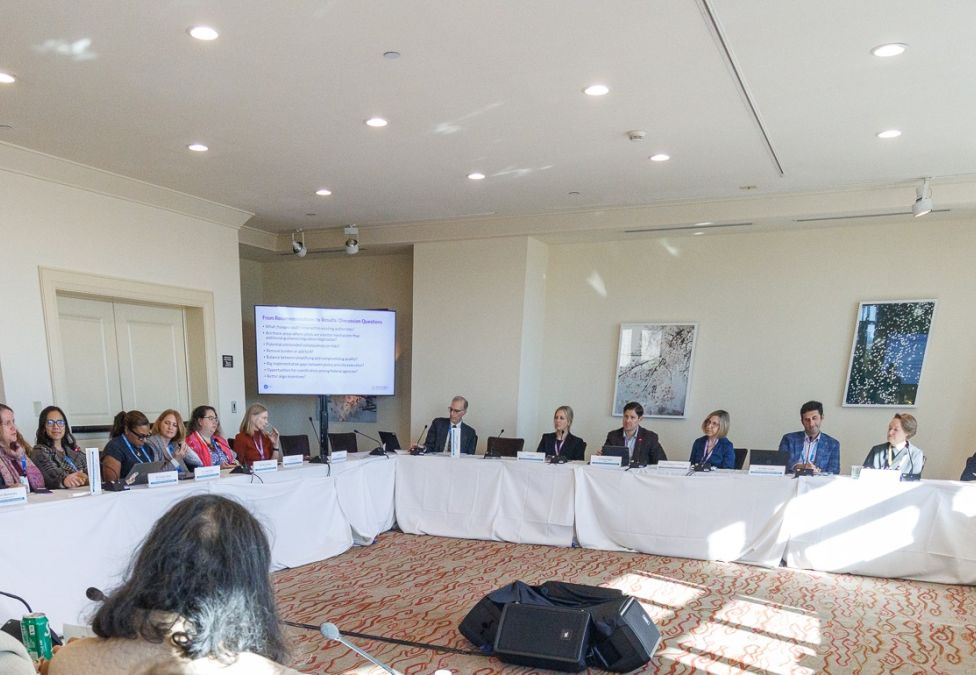 Business meeting with attendees seated at tables facing a panel of speakers in a conference room