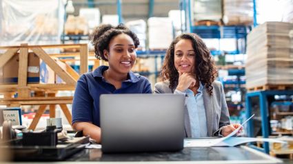 Two women working together at a laptop in a warehouse storage facility