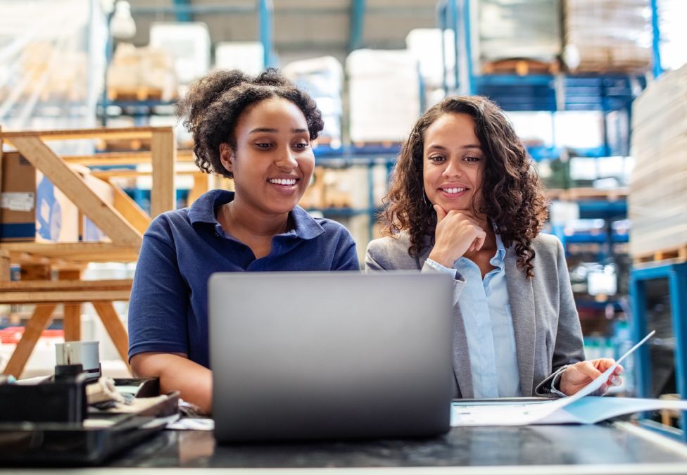Two women working together at a laptop in a warehouse storage facility