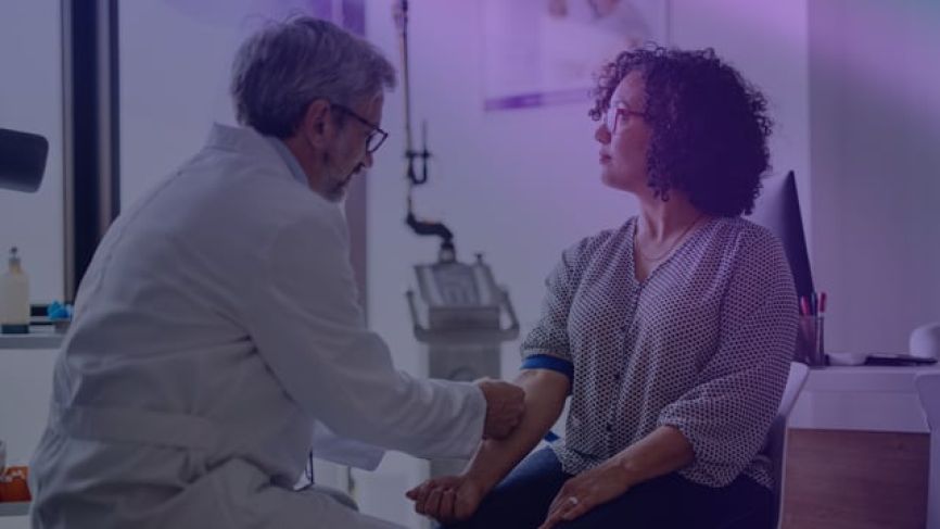 Doctor in white coat consulting with elderly patient in purple sweater in medical office