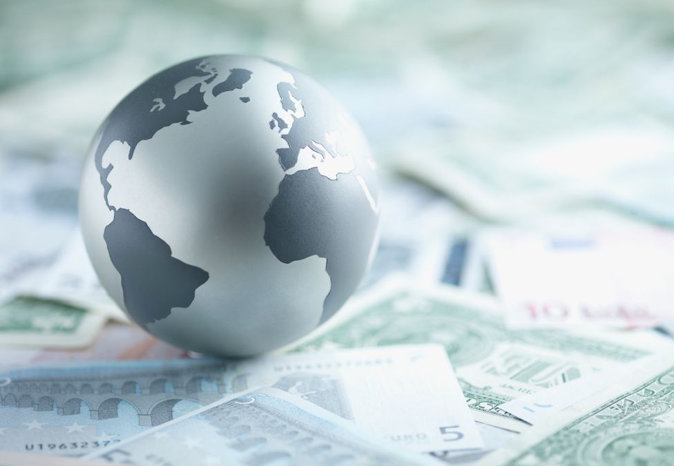 An image of a grayscale globe of Earth sitting upon various paper currencies.