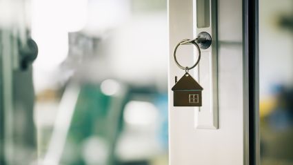 An up close image of a key inside of the lock of a white door with a hanging keychain that is shaped like a house.