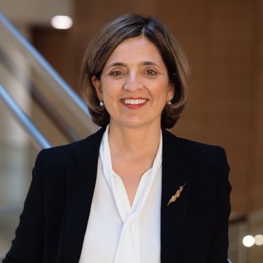 Professional woman in black blazer and white shirt smiling at camera in office setting