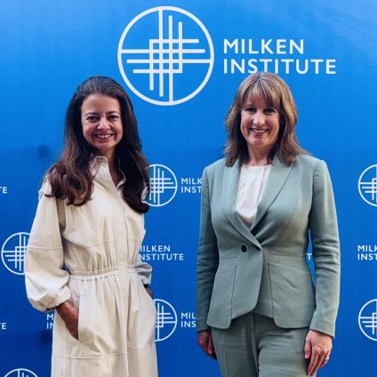 Two women standing together in front of a blue Milken Institute backdrop