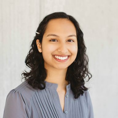 Professional headshot of a smiling woman with curly dark hair wearing a light blue blouse
