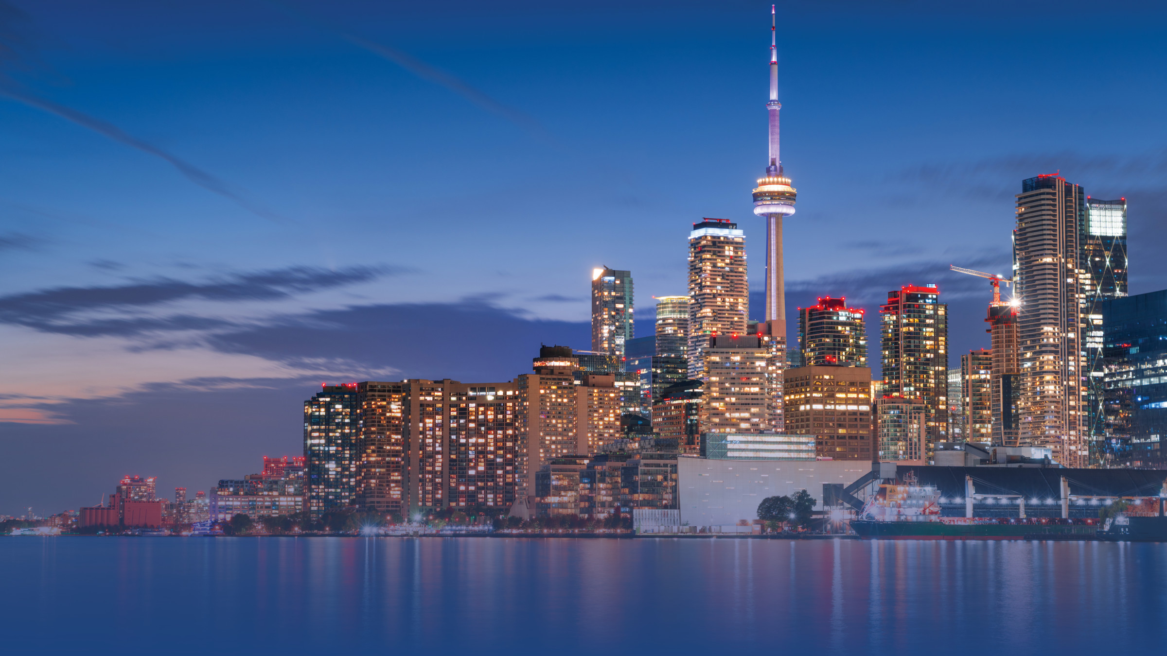 Toronto skyline at dusk with CN Tower and illuminated buildings reflected in Lake Ontario