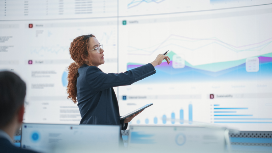 Woman in business attire presenting data charts and graphs on a large display screen
