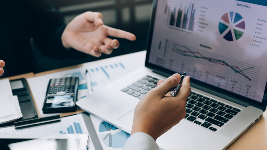 Business professional reviewing financial charts and data on laptop with documents on desk