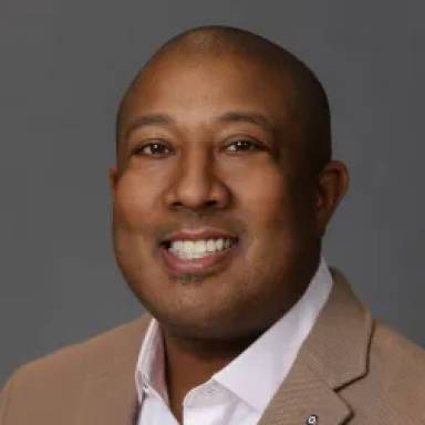Charles “Chuck” Henderson smiling in a beige blazer and white shirt