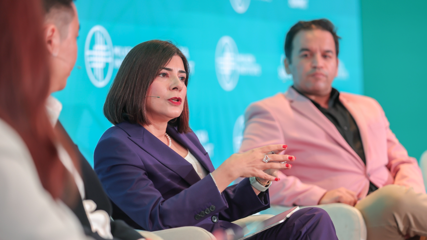 Woman in blue blazer speaking at panel discussion with colleagues against blue backdrop
